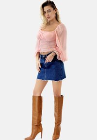 Helles rosa Bluse mit Puffärmeln und Raffung, kombiniert mit einem Denim-Minikilt. Braune kniehohe Stiefel mit Absatz runden den Look ab.