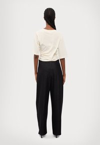 Lys beige kortermet topp med rund hals, kombinert med mørkt stripete vidbukser og en minimal baklomme.