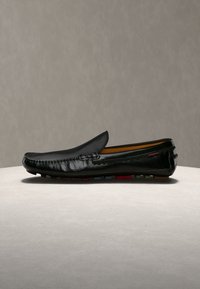 Mocassin en cuir noir avec couture mocassin et semelle en caoutchouc affichant une semelle multicolore, présenté en vue latérale sur une surface claire.