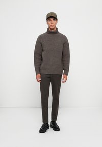 Brun ribbad polotröja, skräddarsydda mörka byxor och en rutig keps, kompletterat med svarta skor. Enkelt och modernt design.