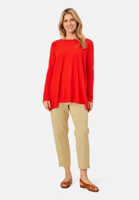 Červený dlouhý rukáv s volným střihem, v kombinaci se světle béžovými kalhotami. Hnědé sandály s řemínky dokončují outfit. Jednoduchý, neformální design.