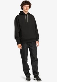 Felpa nera con cappuccio e tasca anteriore, abbinata a jeans scuri. Presenta un cordino di colore a contrasto e una vestibilità casual.