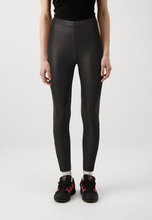 Leggings neri a vita alta con una texture liscia e lucida; abbinati a sneakers nere e rosse, indossati con calzini bianchi alla caviglia.