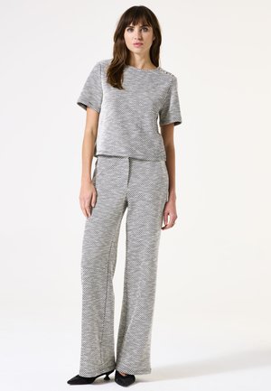 Haut en tricot à motifs gris et blanc associé à un pantalon palazzo assorti, avec une texture douce et des manches courtes. Silhouette ajustée avec un design décontracté.