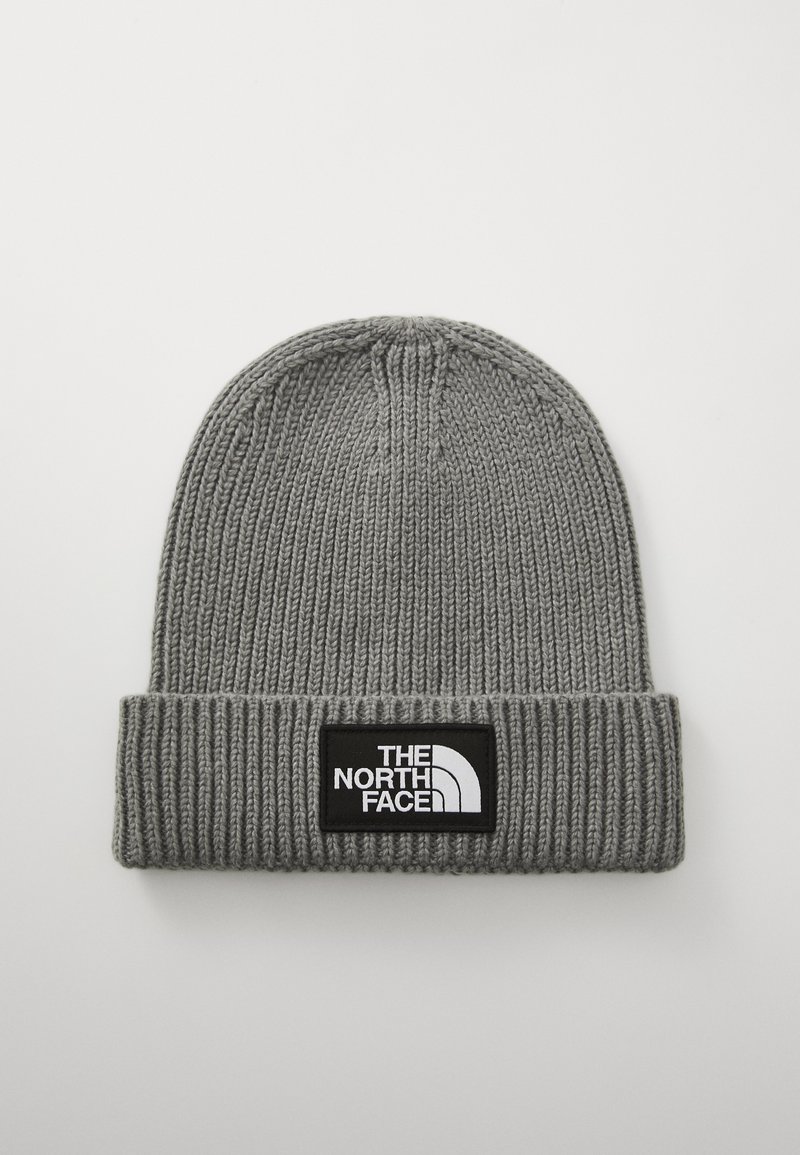 Gorro de punto gris con textura acanalada y un dobladillo vuelto. Presenta un parche rectangular negro con texto y logo en blanco.