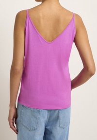 V-ringad, ärmlös rosa tanktopp i mjukt tyg, med avslappnad passform och ren fåll, parat med ljusblå denimjeans.