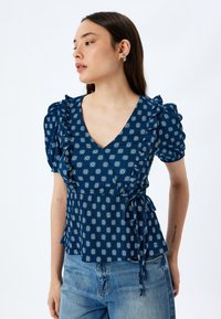 Marineblå blomstret wrap-top med flæser på ærmerne, V-hals og knyt detallering i taljen; lavet af letvægtsstof med en tekstureret finish.