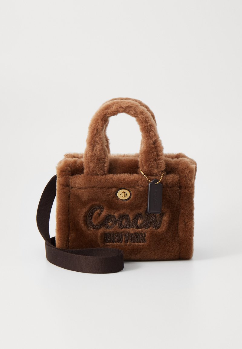 Bolsa de mão em pelo sintético castanho com detalhes em ouro, duas alças curtas, uma alça ajustável e detalhe bordado com o logótipo "Coach New York".