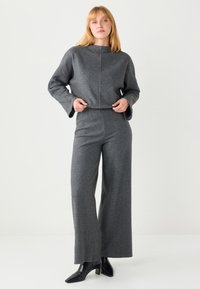 Maglione grigio corto con maniche larghe e scollo dritto abbinato a pantaloni grigi a gamba larga, completato da stivaletti neri con tacco largo.