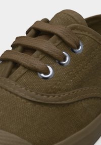 Καφέ πάνινο αθλητικό παπούτσι με χοντρές κορδόνια που περνούν μέσα από ασημένιους μεταλλικούς οφθαλμούς και ορατή ραφή κατά μήκος της επάνω άκρης.