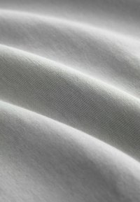 Világosszürke szövet, sima textúrával, apró redőkkel és ráncokkal. A szövés szoros és egyenletes, lágy fényt ver vissza.