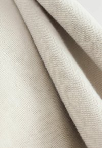 Heller beiger Stoff mit einer weichen Textur und einem feinen Strickmuster, das eine leicht erhabene Oberfläche und subtile Farbvariationen aufweist.