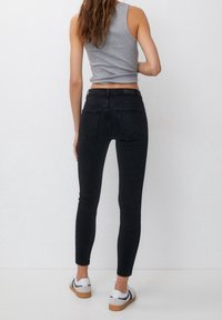 Vaqueros negros ajustados de cintura alta, con un diseño de bolsillo trasero, combinados con zapatillas blancas y una camiseta gris sin mangas.