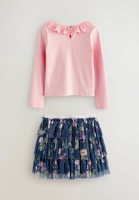 Rosa Langarmshirt mit Rüschensaum am Ausschnitt und einem Schlitzdetail, kombiniert mit einem marineblauen Tüllrock mit Blumenmuster und gestuften Rüschen.