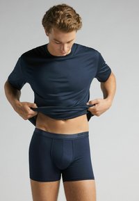 Námořnická modrá sportovní tričko vyrobené z hladké, elastické látky; přiléhavý střih. Shodné námořnické boxerky s označeným pasem, bezešvý design.