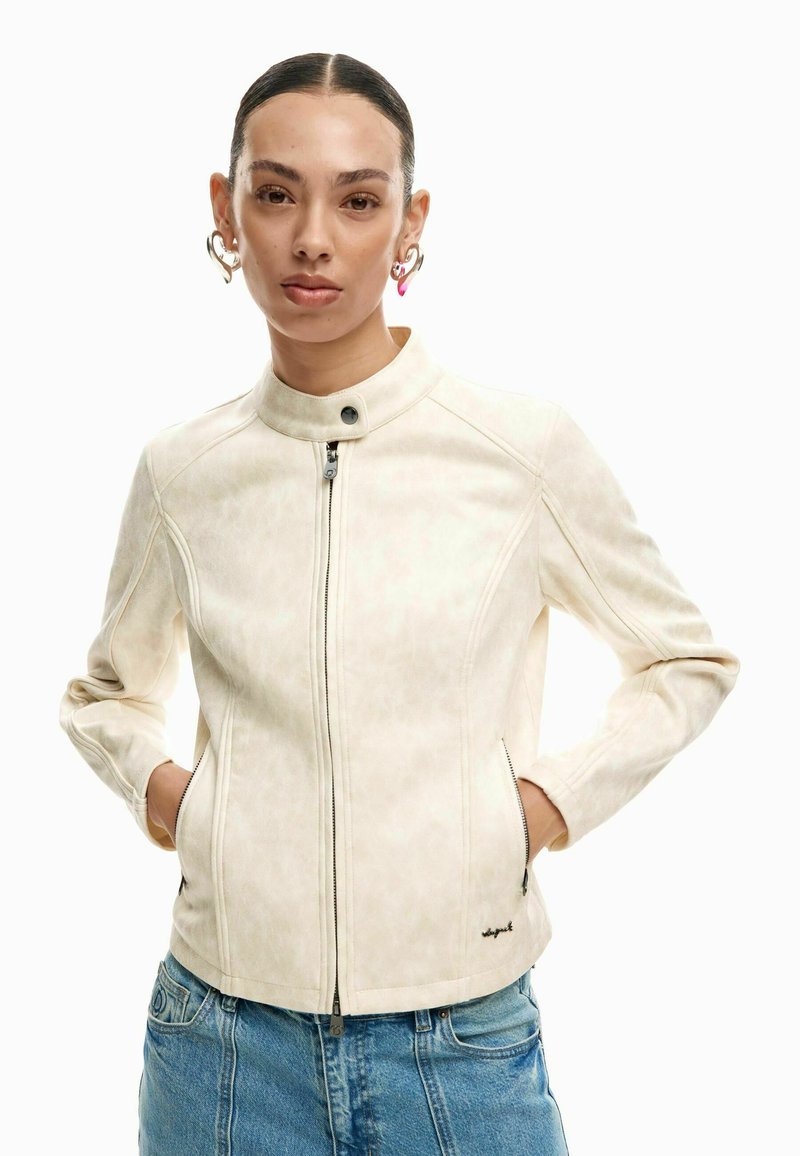 Világos bézs dzseki magas gallérral, elöl cipzárral és testhezálló szabással. Finoman texturált, sima anyagból készült, oldalán zsebekkel.