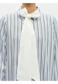 Gros plan sur une personne portant une chemise à rayures bleues et blanches avec un grand nœud blanc attaché au col.