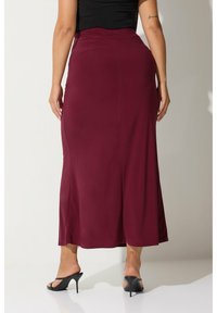 Burgundyröd långkjol i figurnära passform, tillverkad av elastisk tyg, med en mjuk textur och en diskret utvidgning vid nederkanten, kombinerad med svarta klackar.