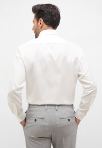 Witte lange mouwen overhemd met een gespreide kraag, gecombineerd met lichtgrijze broek met twee achterzakken en subtiele streepjes.