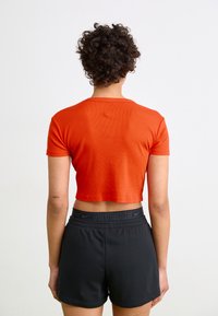 Rød crop-top med korte ermer, ribbet tekstur. Kombinert med svarte treningsshorts med elastisk midje og logo-detalj.
