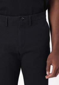 Black cotton trousers with a smooth texture, featuring a front button closure and belt loops. The design includes tapered legs and side pockets.