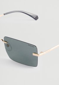 Napapolan aurinkolasit, joissa on suorakulmaiset harmaat linssit, kultainen metallikehys, ohuet varret ja huomaamaton brändäys linssissä ja varressa.