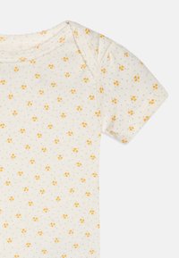 Bodysuit en coton à manches courtes couleur crème avec un motif floral jaune et des pois verts, présentant une texture côtelée et un encolure arrondie.