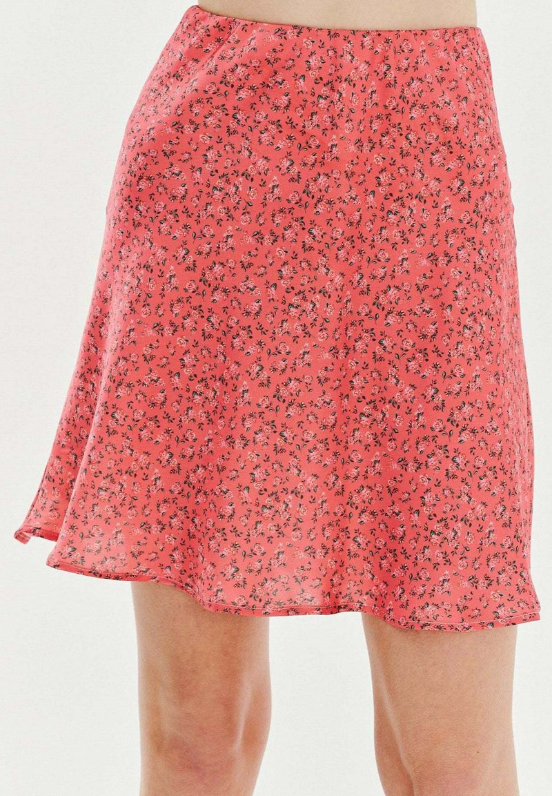 Červená sukně s květinovým vzorem vyrobená z lehké tkaniny, s rozšířeným střihem a lemem, který se jemně vlní, s malými černými detaily.