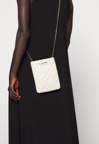 Borsa crema trapuntata con tracolla a catena, forma rettangolare e dettagli in metallo dorato. Presenta una placca con logo sulla parte anteriore.