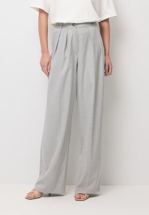 Kobieta ubrana w jasnoszare, szerokie spodnie z wysokim stanem i plisami, w połączeniu z białym, krótkim topem i beżowymi sandałami na obcasie z odkrytymi palcami.