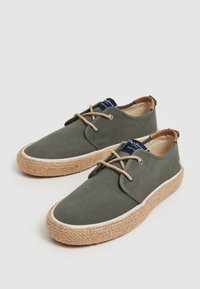 Zapatos de lona verdes con suela de yute trenzado, detalles en marrón y cordones beige, con un diseño bajo y puntera redonda.
