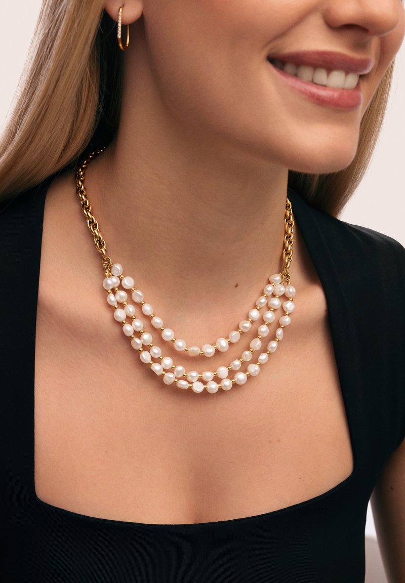 Collar de múltiples hilos con perlas blancas y acentos en tono dorado, que presenta un diseño de cadena gruesa y una apariencia en capas sobre una blusa negra.