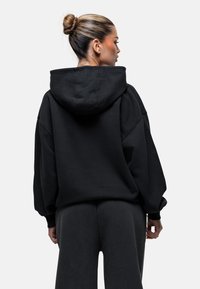 Zwarte oversized hoodie met een kangoeroezak, capuchon en geribde manchetten, aangevuld met bijpassende donkere trainingsbroek. Zachte, textuurrijke stof.