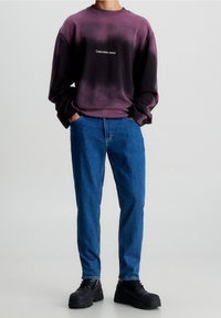 Svetr s purpurovým gradientem a logem "Calvin Klein Jeans", zkombinovaný s modrými džíny a černými platformovými botami. Neformální, volný střih.