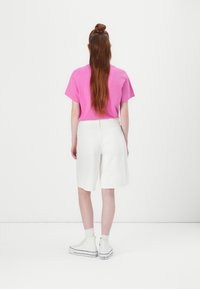Rosa kortermet skjorte, hvite denimshorts og hvite høye sneakers. Langt brunt hår stylet i en halv oppsatt knute. Enkel, uformell antrekk.