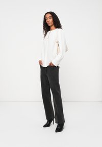 Witte lange mouwen top met een lichte opening bij de hals, gecombineerd met zwarte flared jeans en zwarte hoge laarzen. Eenvoudig ontwerp en texturen.