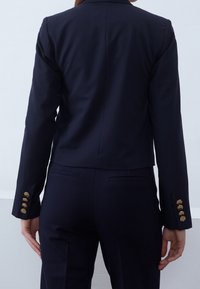 Blazer bleu marine à coupe ajustée. Caractéristiques : design raccourci, texture lisse et boutons dorés sur les manches.