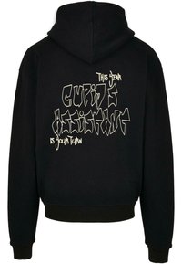Fekete kapucnis felső bordázott mandzsettával és hem vesszők, hátulja feltűnő fehér graffitistílusú szöveggel: "Idén Cupido segítője a te köröd."