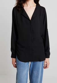 Black long-sleeve shirt with a V-neck collar, button-down front, and relaxed fit, paired with light blue wide-leg jeans. Smooth fabric texture.