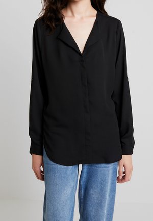 Maglietta nera a maniche lunghe con colletto a V, chiusura con bottoni e vestibilità comoda, abbinata a jeans a gamba larga blu chiaro. Tessuto morbido.