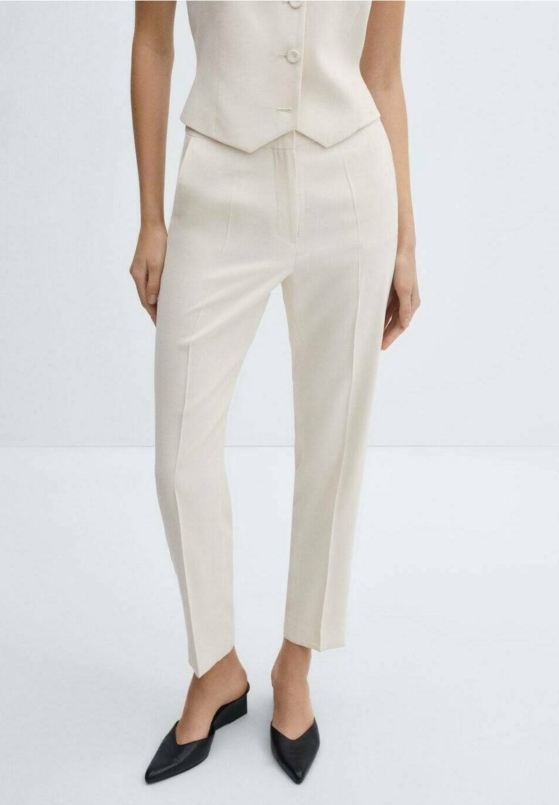 Beige kalhoty na míru se rovný střihem, se středně vysokým pasem a předními záhyby. Hladká, lehká tkanina; v kombinaci s černými muly.