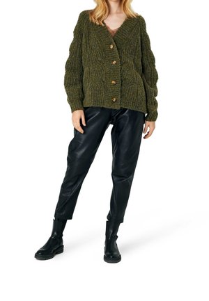 Oliwkowo zielony dziergany kardigan z fakturowanym wzorem, dużymi guzikami i dekoltem w serek. Połączony z czarnymi skórzanymi spodniami i botkami za kostkę.