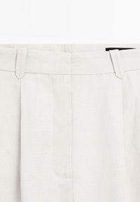 Gros plan sur la taille d'un pantalon blanc avec passants pour ceinture et fermeture éclair avant dissimulée.