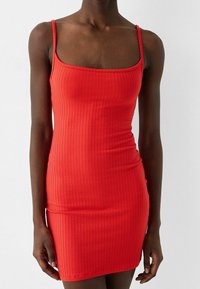 Robe rouge sans manches à côtes avec un décolleté carré. Coupe ajustée mettant en valeur la silhouette, avec une texture lisse et des accents minimalistes.