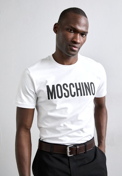 Tricou alb din bumbac cu text îndrăzneț negru "MOSCHINO", mâneci scurte și guler rotund, asortat cu o curea din piele maro.