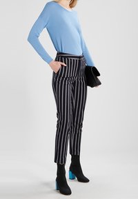 Ljusblå långärmad topp i kombination med svart och vit randig högmidjad byxa. Svarta ankelstövlar med blå klackar. Svart clutch.