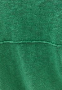 Tessuto verde con una sottile trama, caratterizzato da una cucitura orizzontale di filo coordinato al centro. Nessun motivo o dettaglio distintivo visibile.