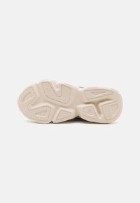 Semelle de chaussure de sport en beige clair, présentant une surface en caoutchouc texturée avec des motifs de semelle variés et des sections découpées pour une meilleure traction.