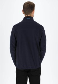 Dunkelblaue Fleecejacke mit hohem Kragen, ausgestattet mit einer strukturierten Oberfläche und einem dezenten Logo auf dem Rücken. Schlichtes, funktionales Design.