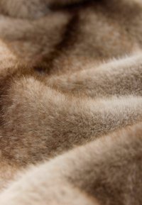 Close-up of soft, light brown and beige fur fabric with fine, dense texture and natural color gradients in folds.
